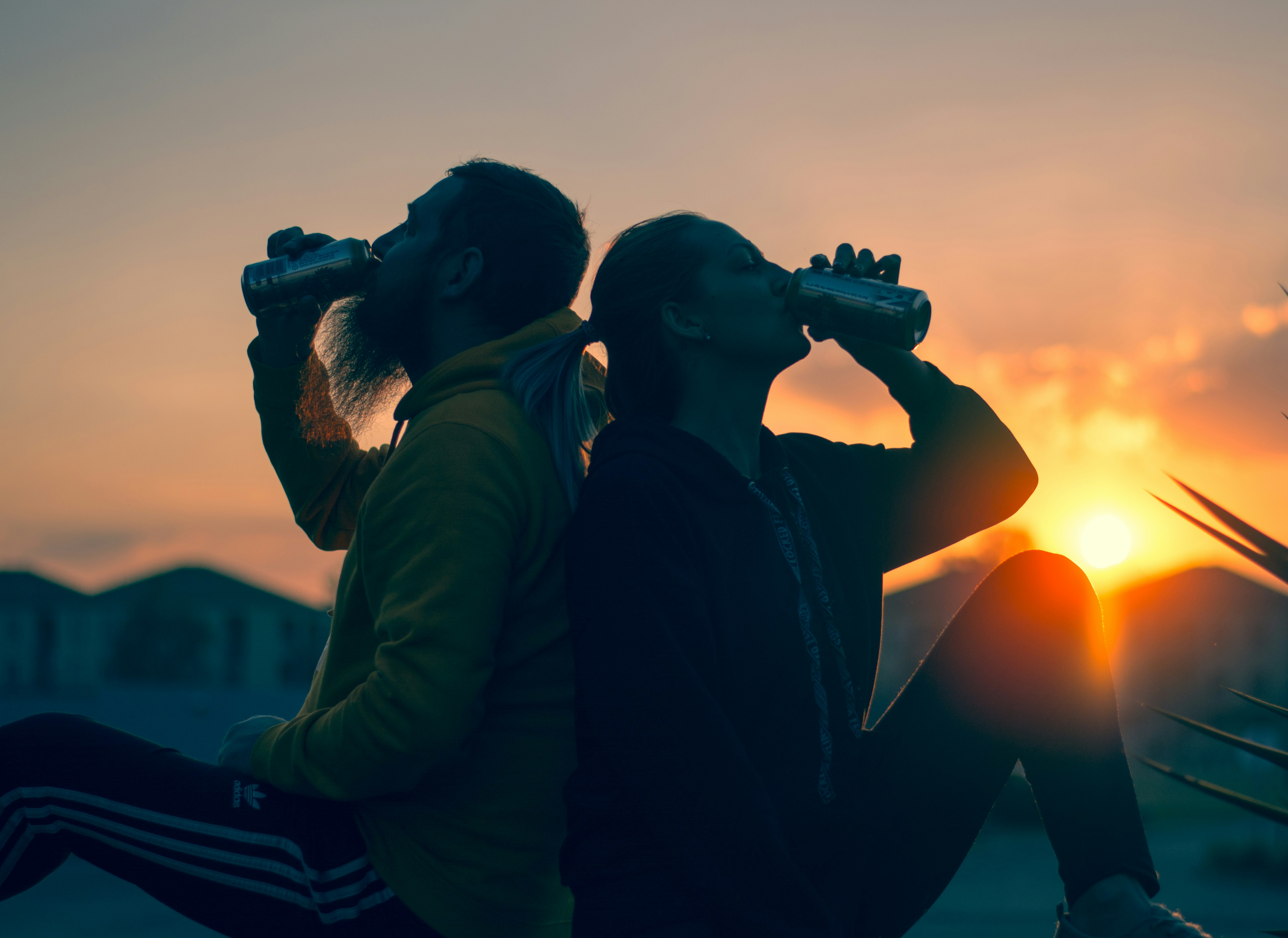 Close up of diverse young adults toasting with amber drinks in reusable eco-cups at an outdoor sunset party.