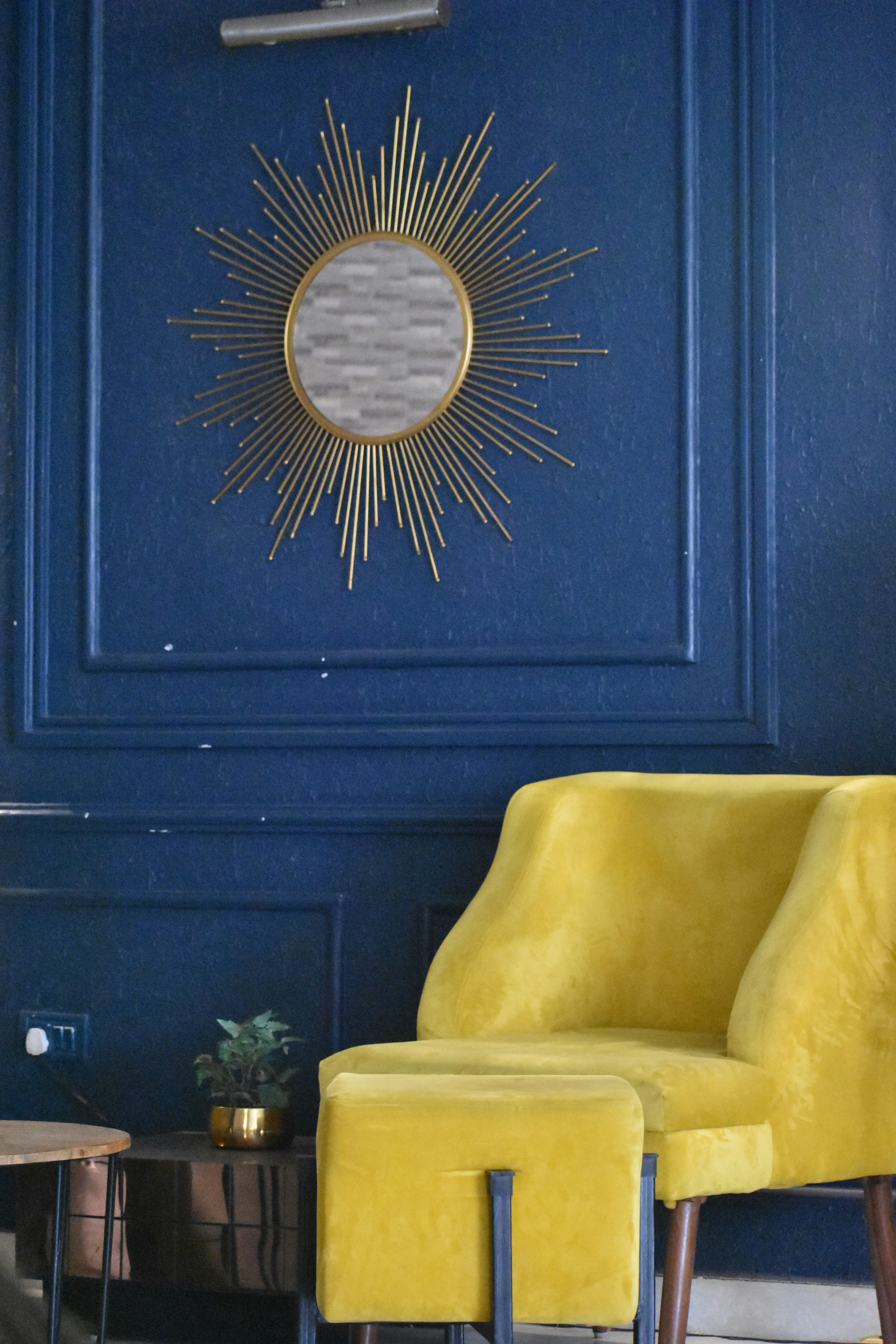 Close up of Art Deco style wallpaper pattern with gold geometric lines on dark blue background next to a velvet armchair