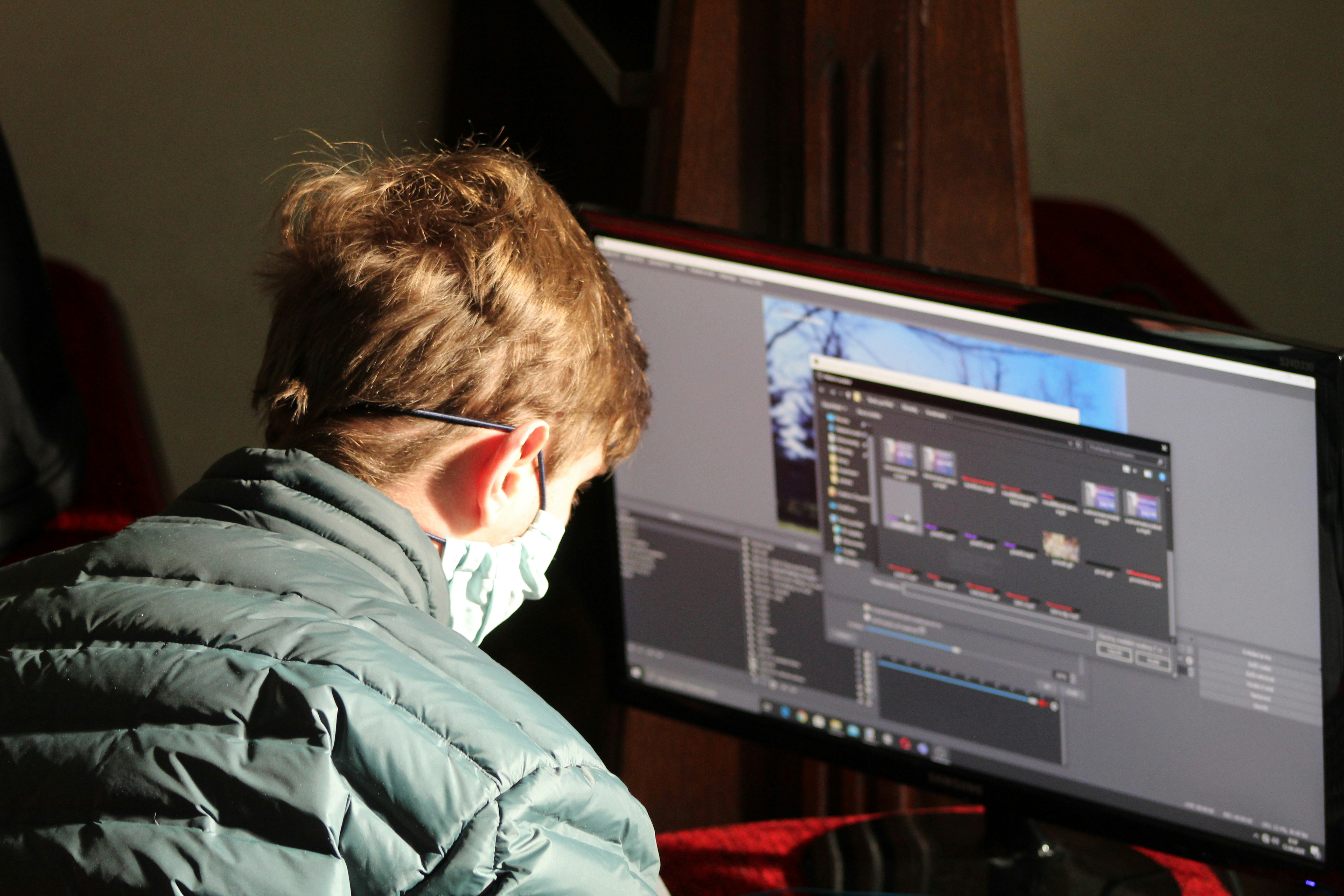 Film editor working on a dual monitor setup with video timeline software visible