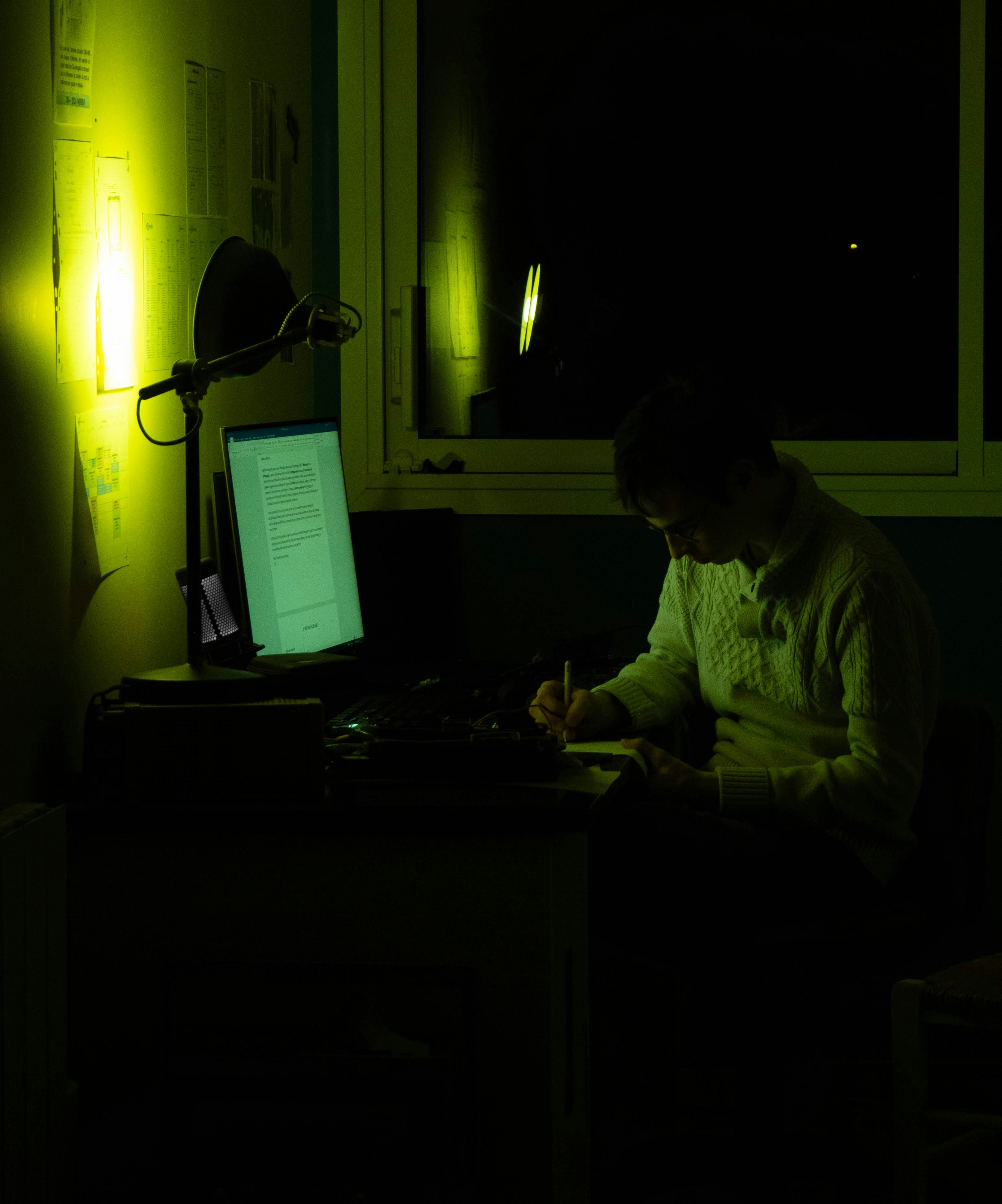 A musician working on a laptop in a home studio with neon lighting