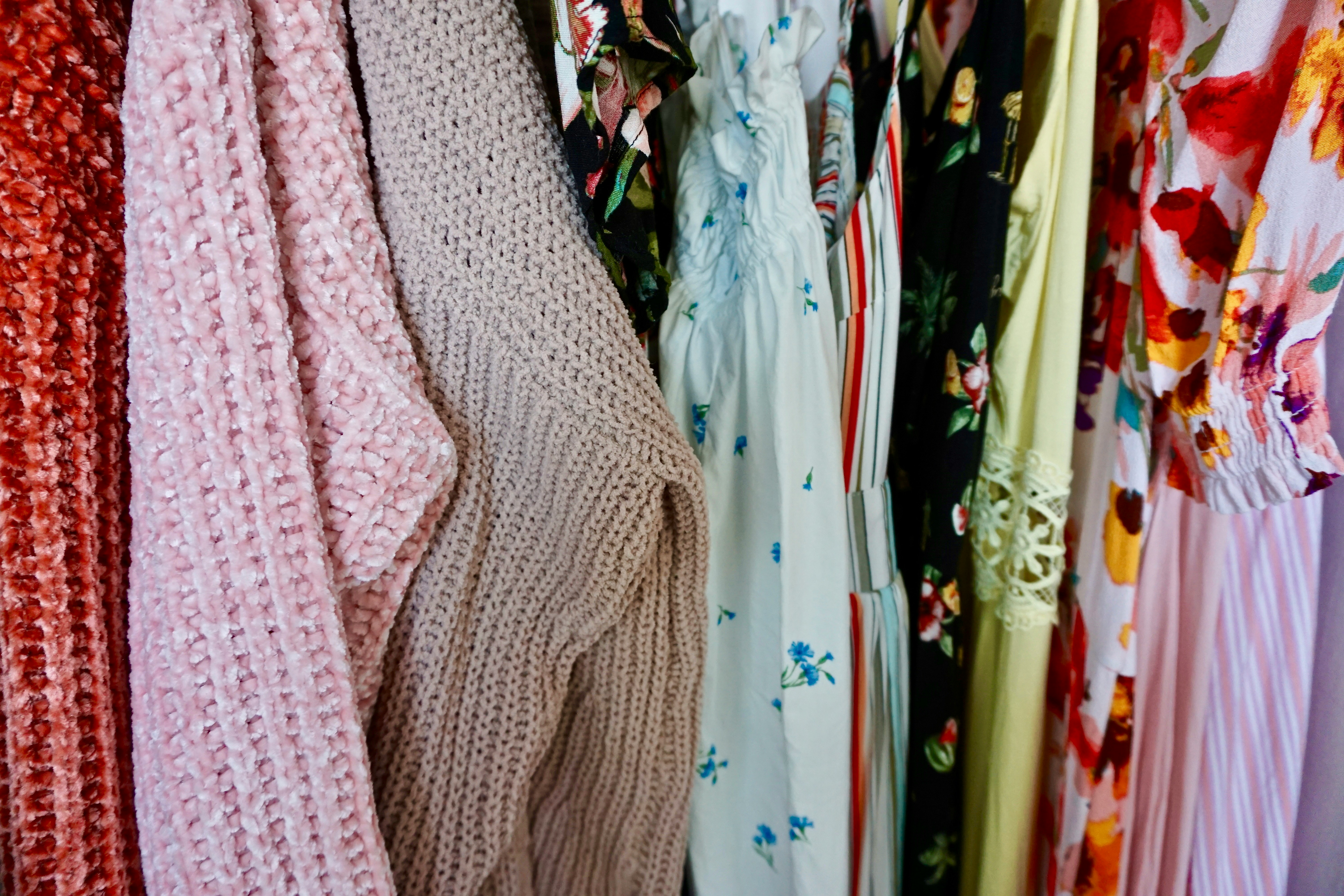 High quality photo of a rack of clothes showing a mix of vintage denim, soft knits, and floral dresses in a bright boutique setting