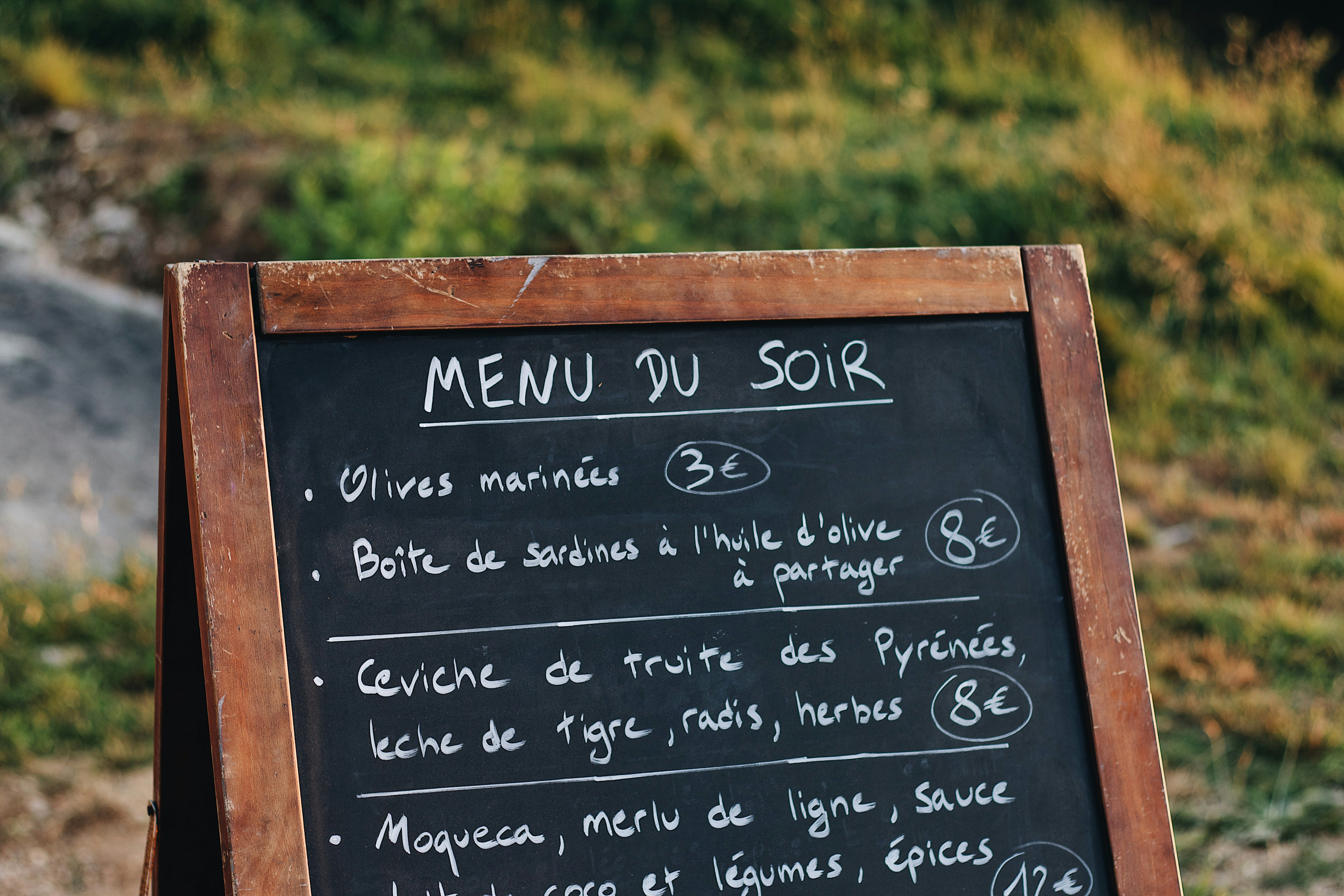 Menu du jour sur ardoise avec prix en francs suisses à côté d'un verre de vin sur une table de restaurant
