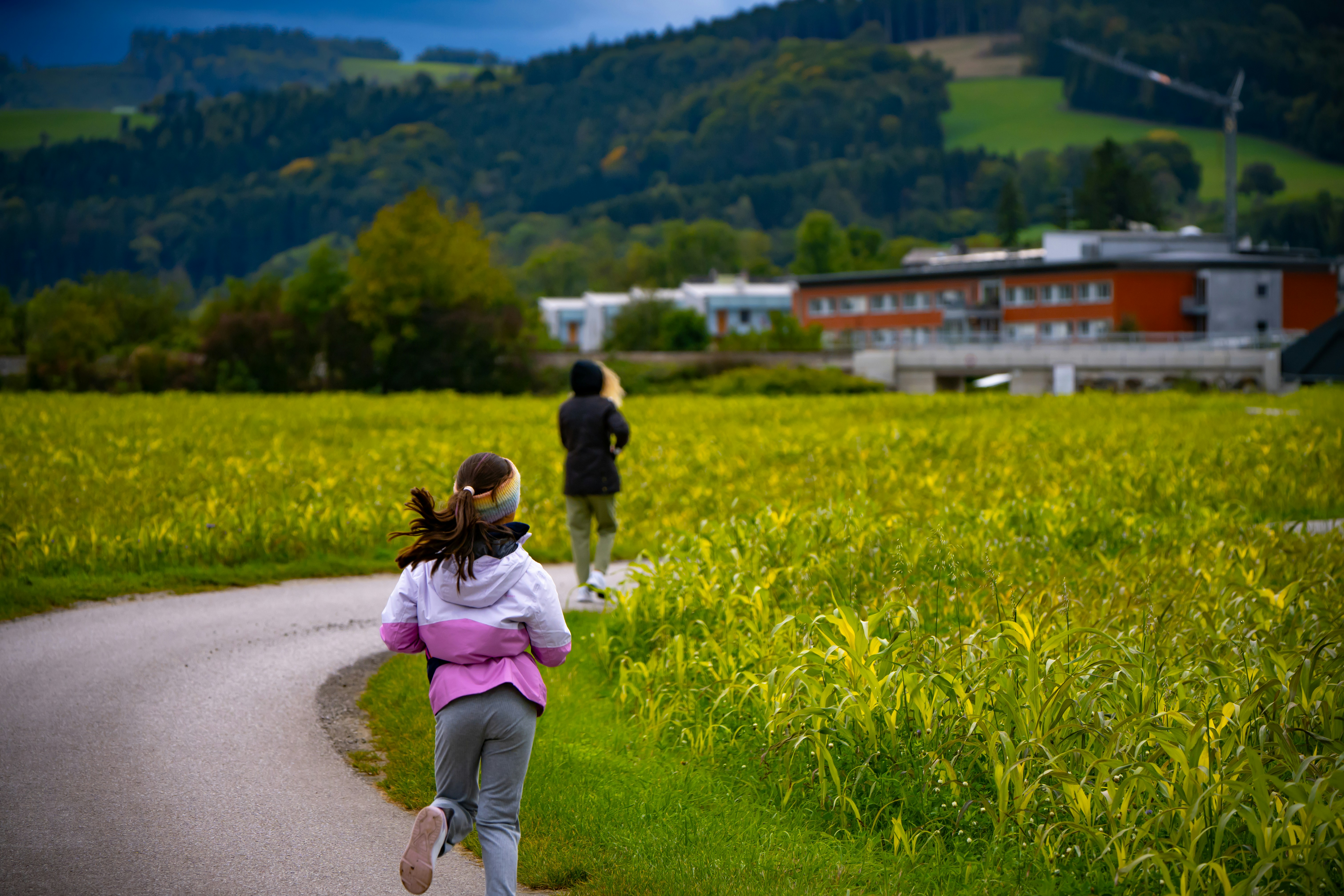 Group of diverse schoolchildren sitting casually on grass outdoors with a scenic Swiss landscape background, smiling naturally toward the camera.