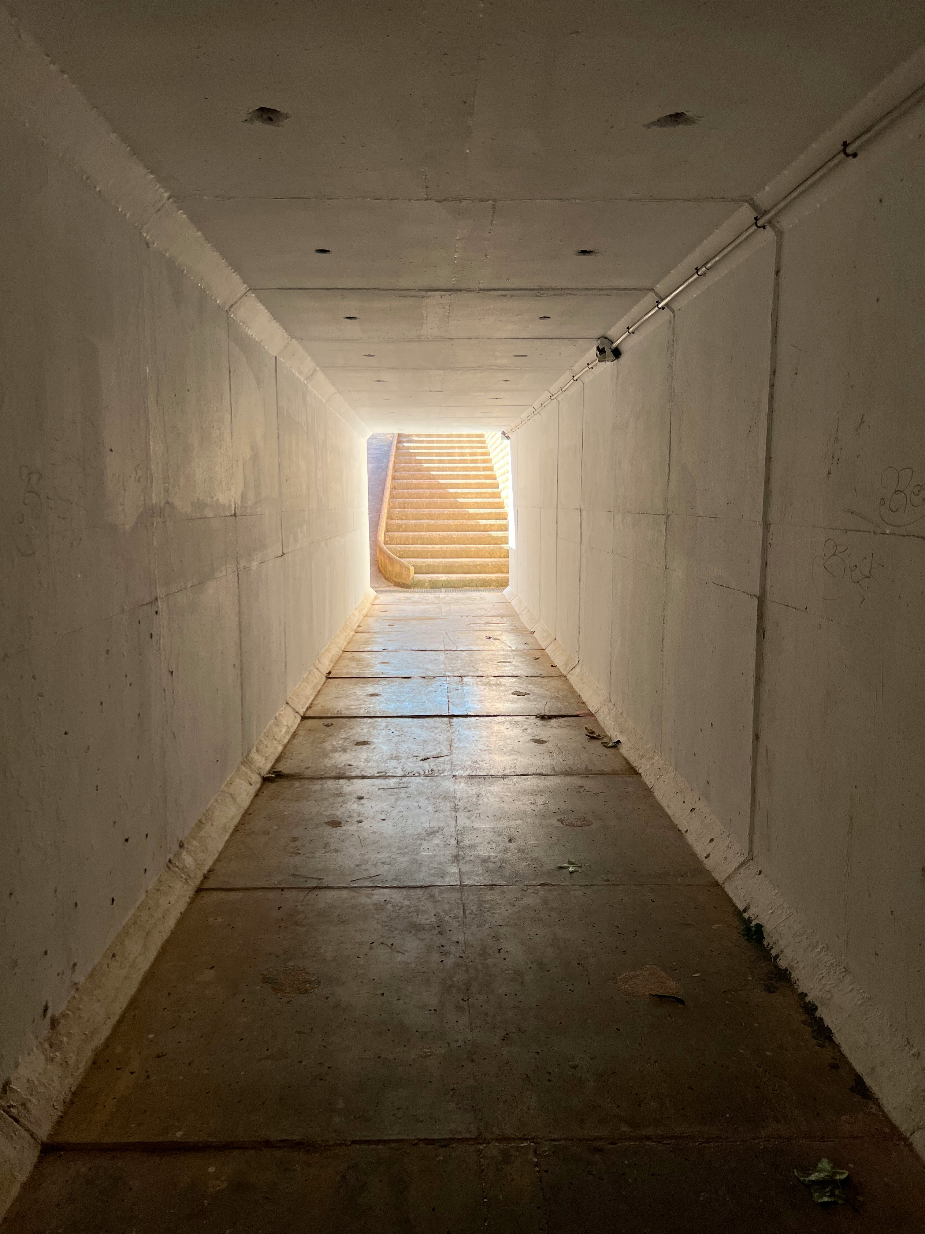 Minimalist wall sconces and a suspended pendant light illuminating a narrow hallway with light beige walls