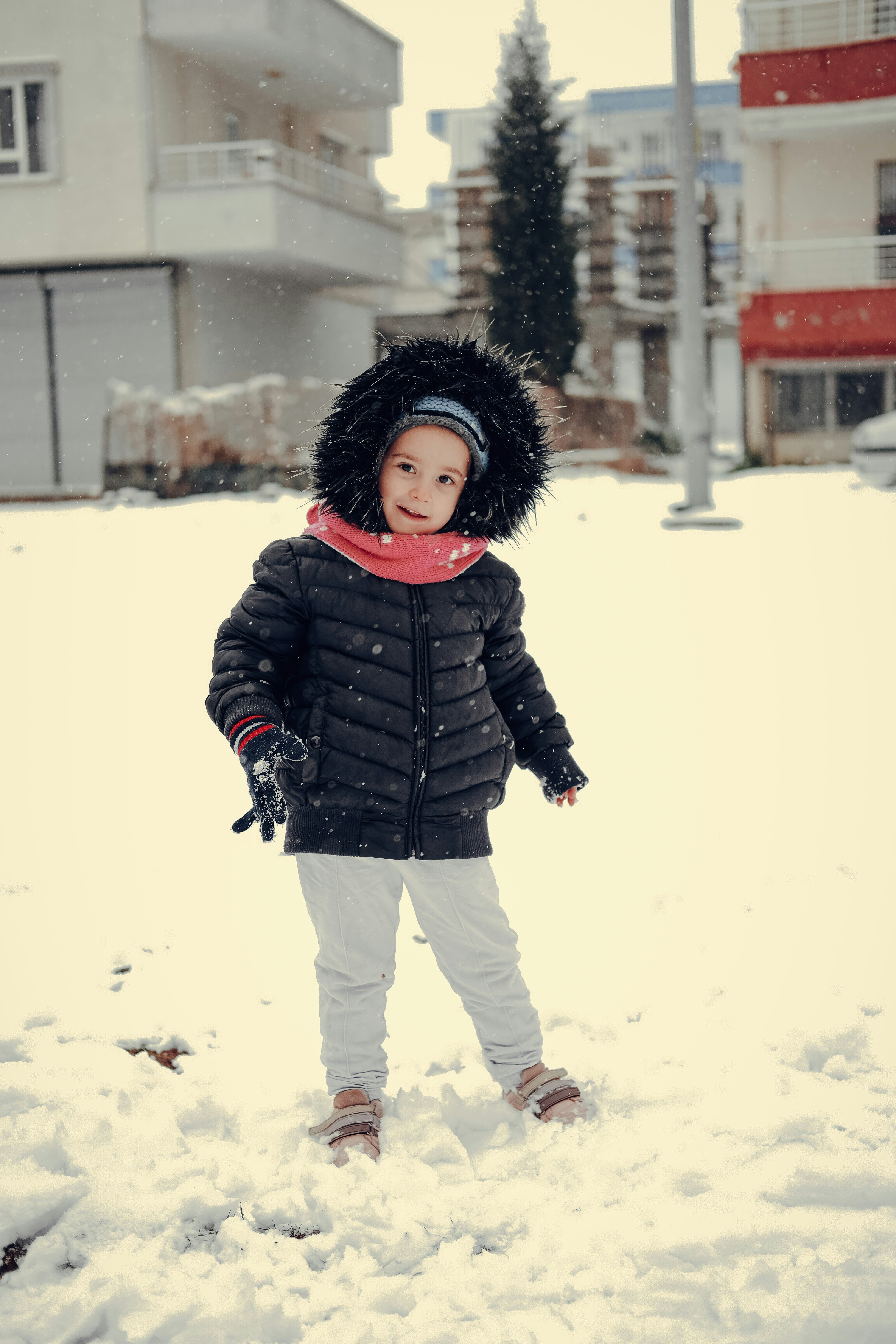 Enfant en tenue d'hiver jouant avec la neige lors d'une séance photo sur les hauteurs du Jura vaudois, lumière douce hivernale
