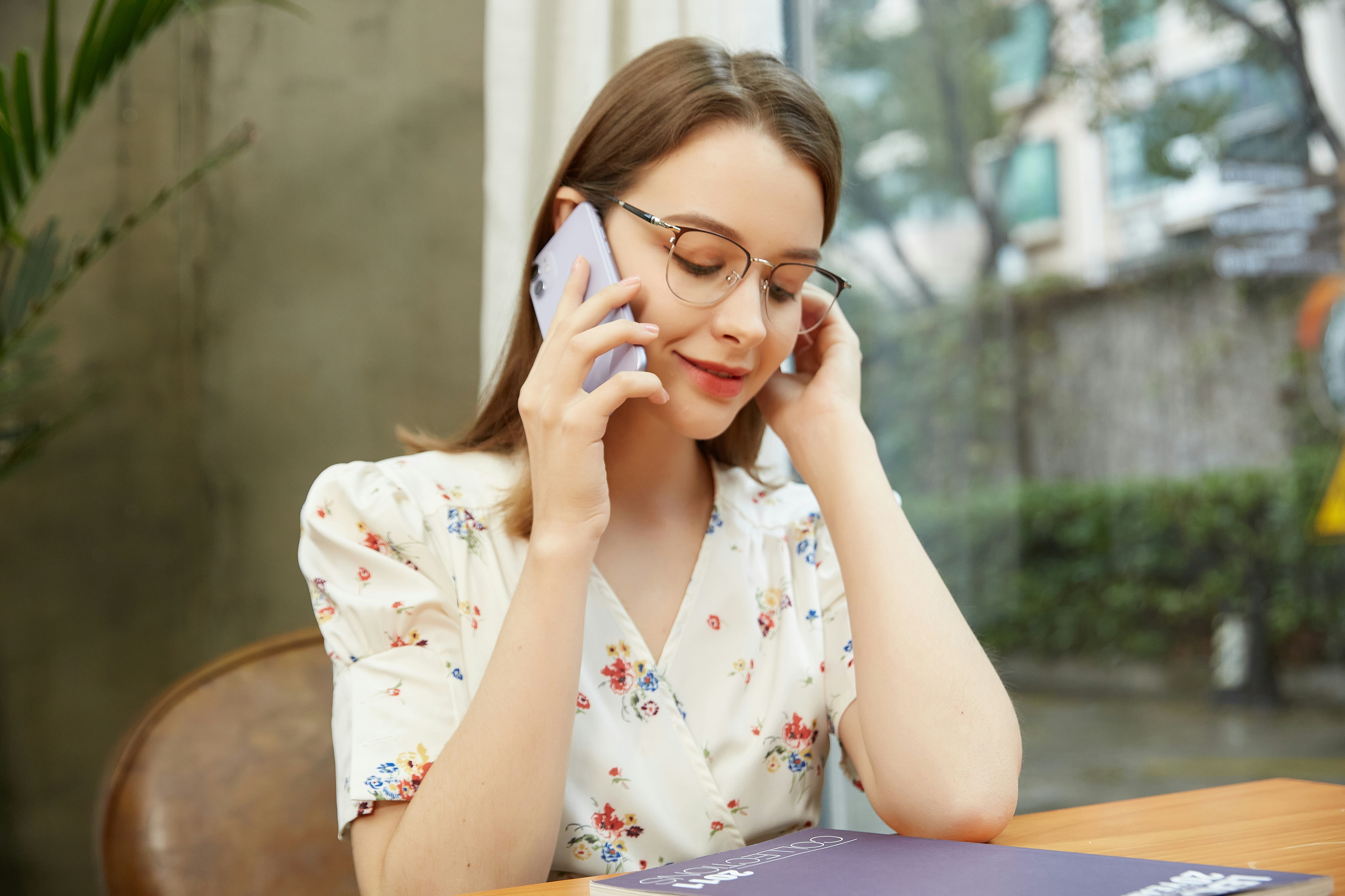 Person making a phone call looking concerned while holding insurance papers near a window