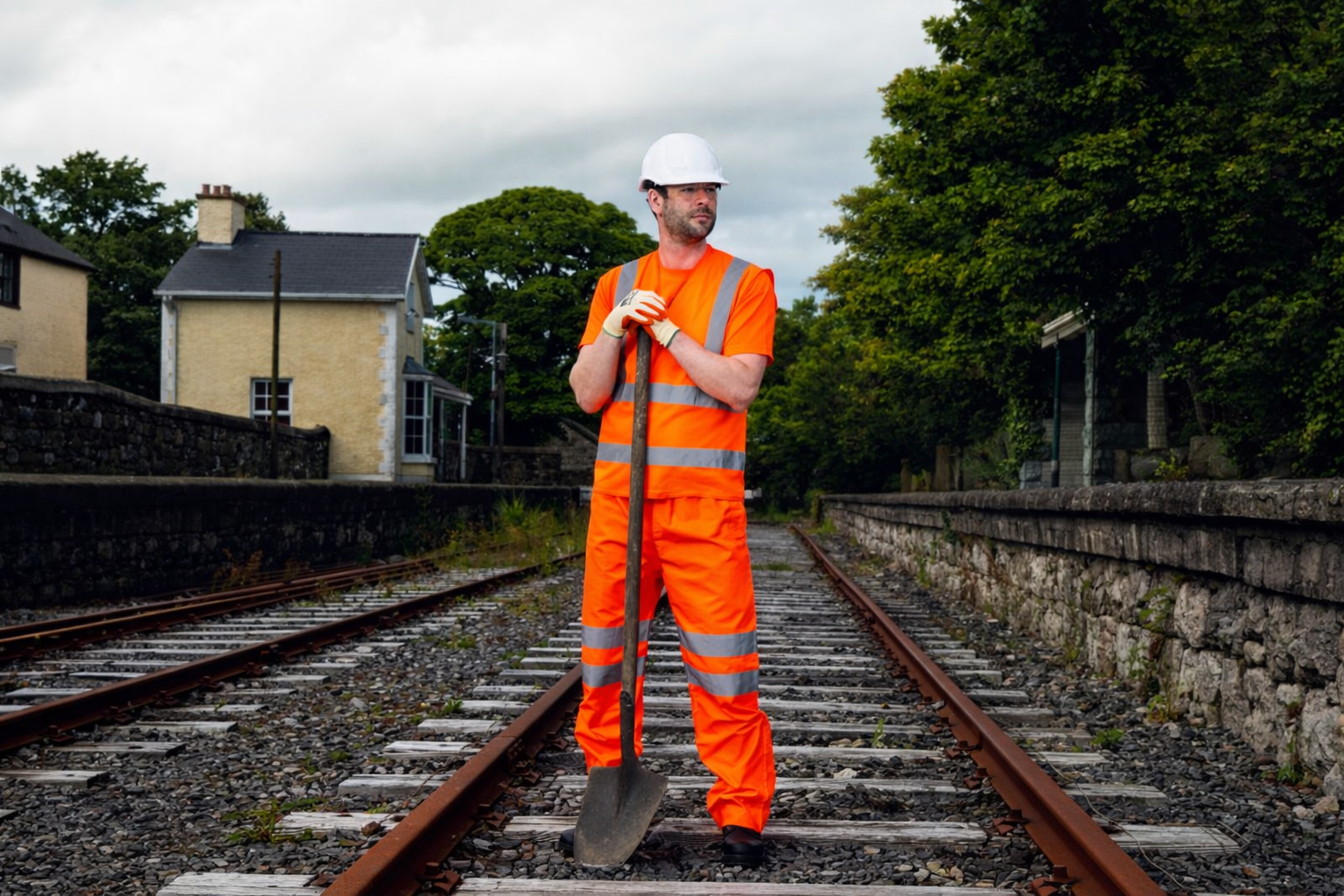 Homme portant un gilet haute visibilité orange Portwest sur un chemin de fer avec un pelle à la main