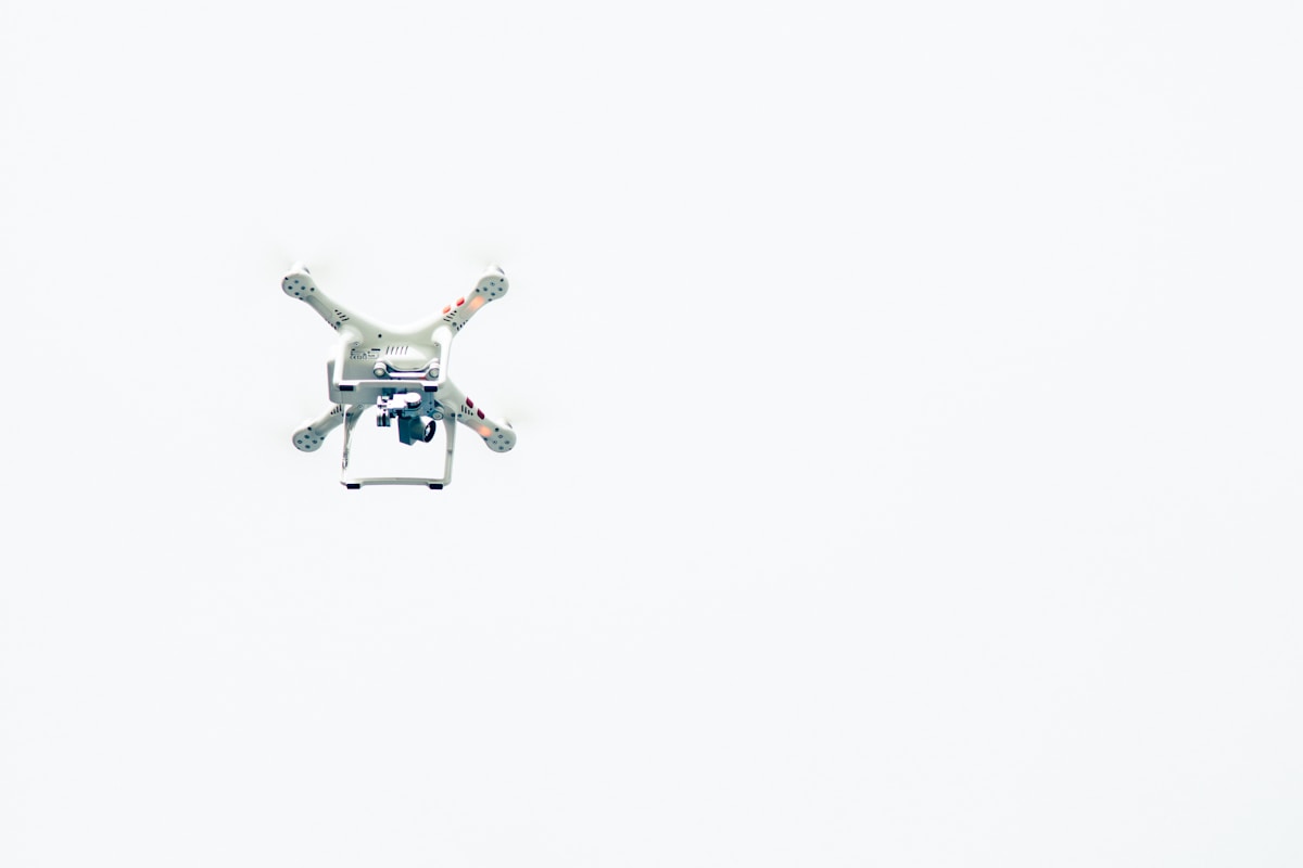Drone quadrirotor blanc avec caméra, flottant sur fond blanc.