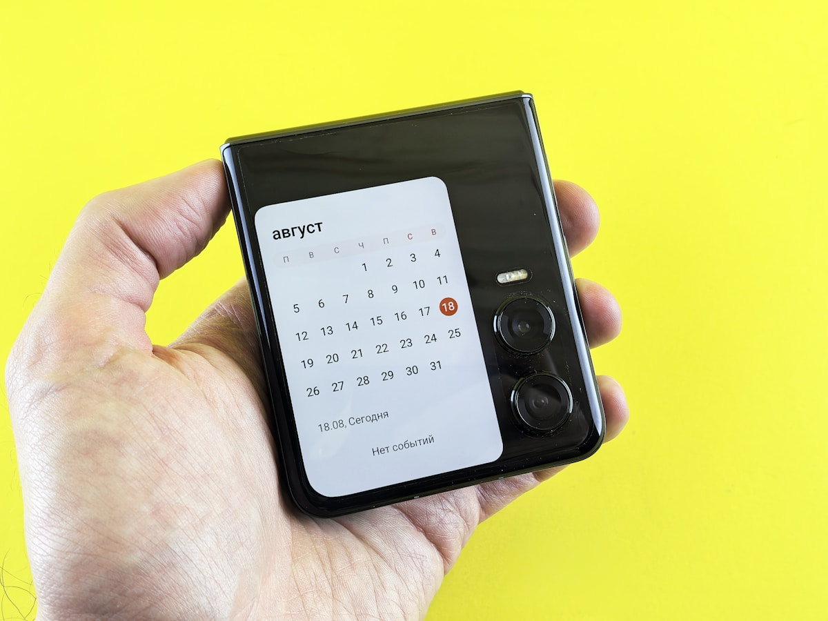 A hand holds a phone displaying a calendar.