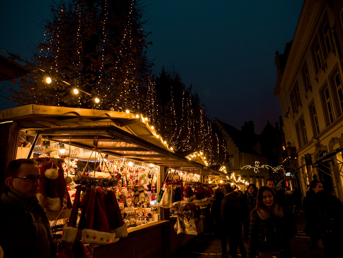 Marché de Noël illuminé la nuit, avec des étals décorés et des visiteurs.