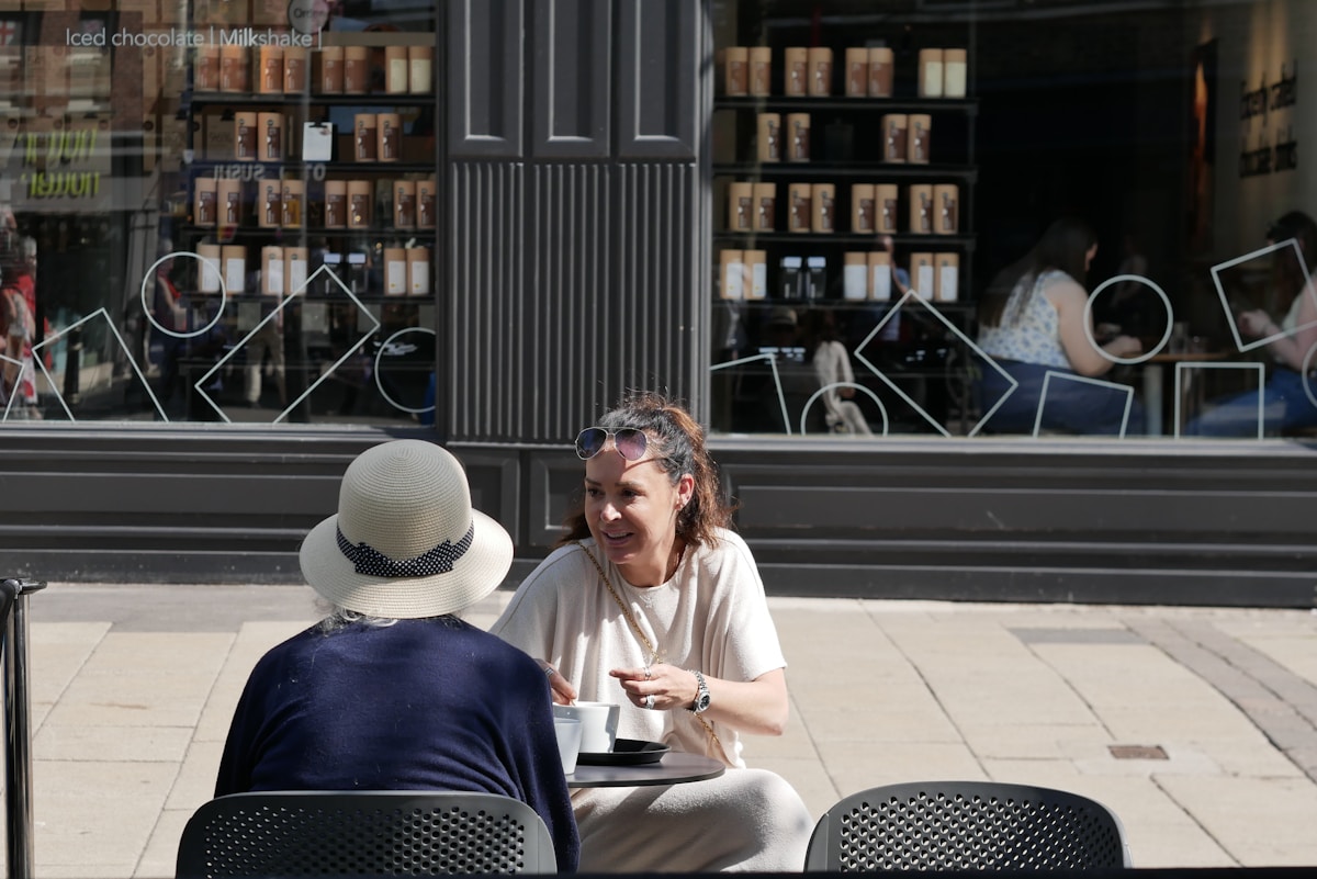 Deux personnes assises à une table de café, discutant et profitant du soleil.