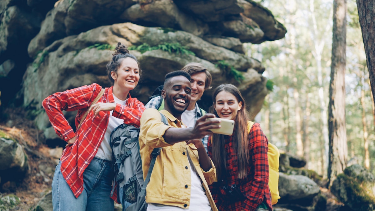 Groupe d'amis souriants prenant un selfie dans un paysage forestier.