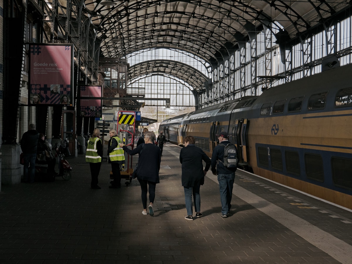 Gare ferroviaire avec arche en métal, passagers et personnel.