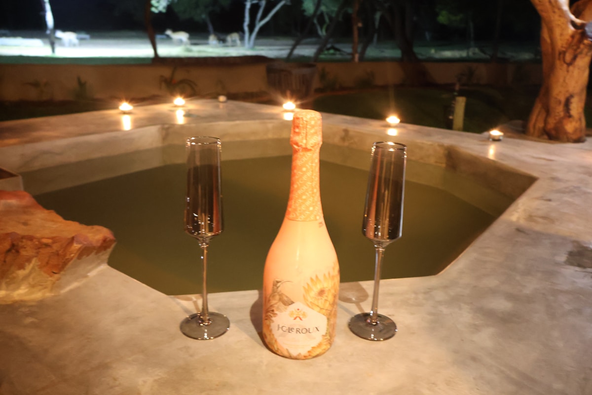 Bouteille de vin, verres de champagne, lumières tamisées, piscine, nuit.