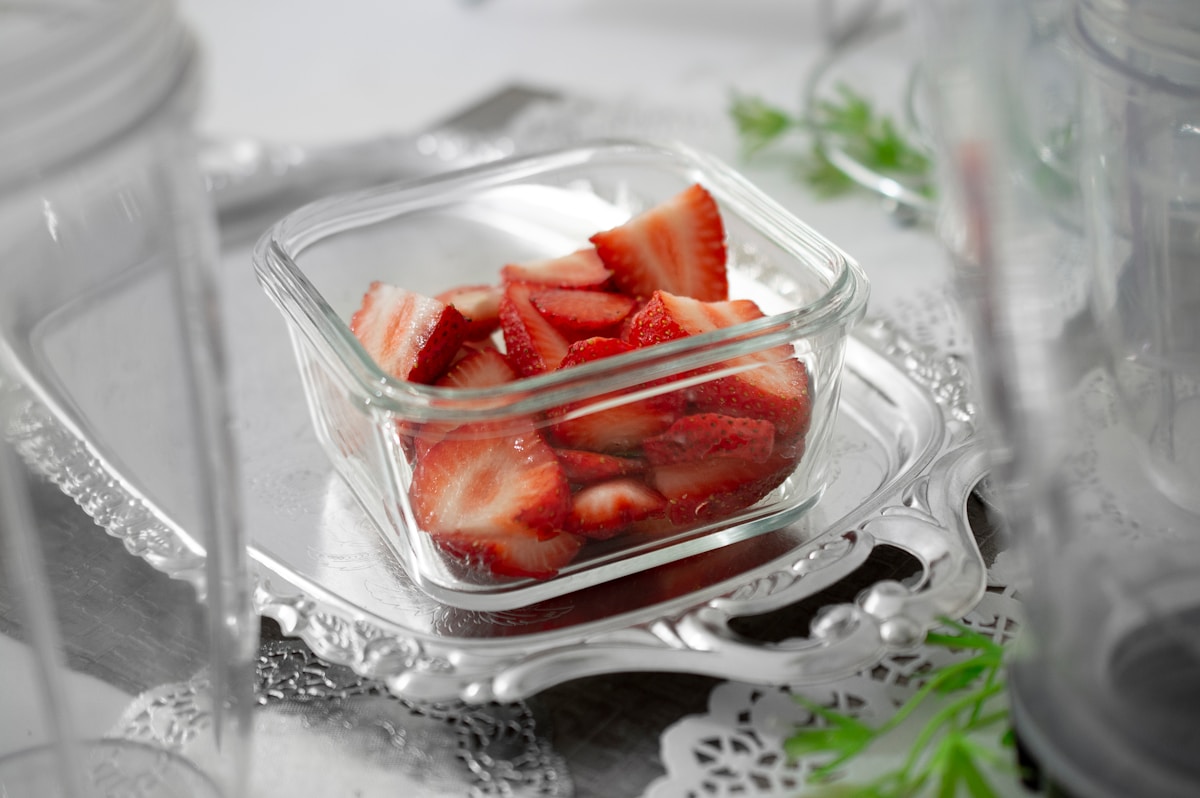 Fraises fraîches tranchées dans un bol en verre sur un support argenté.