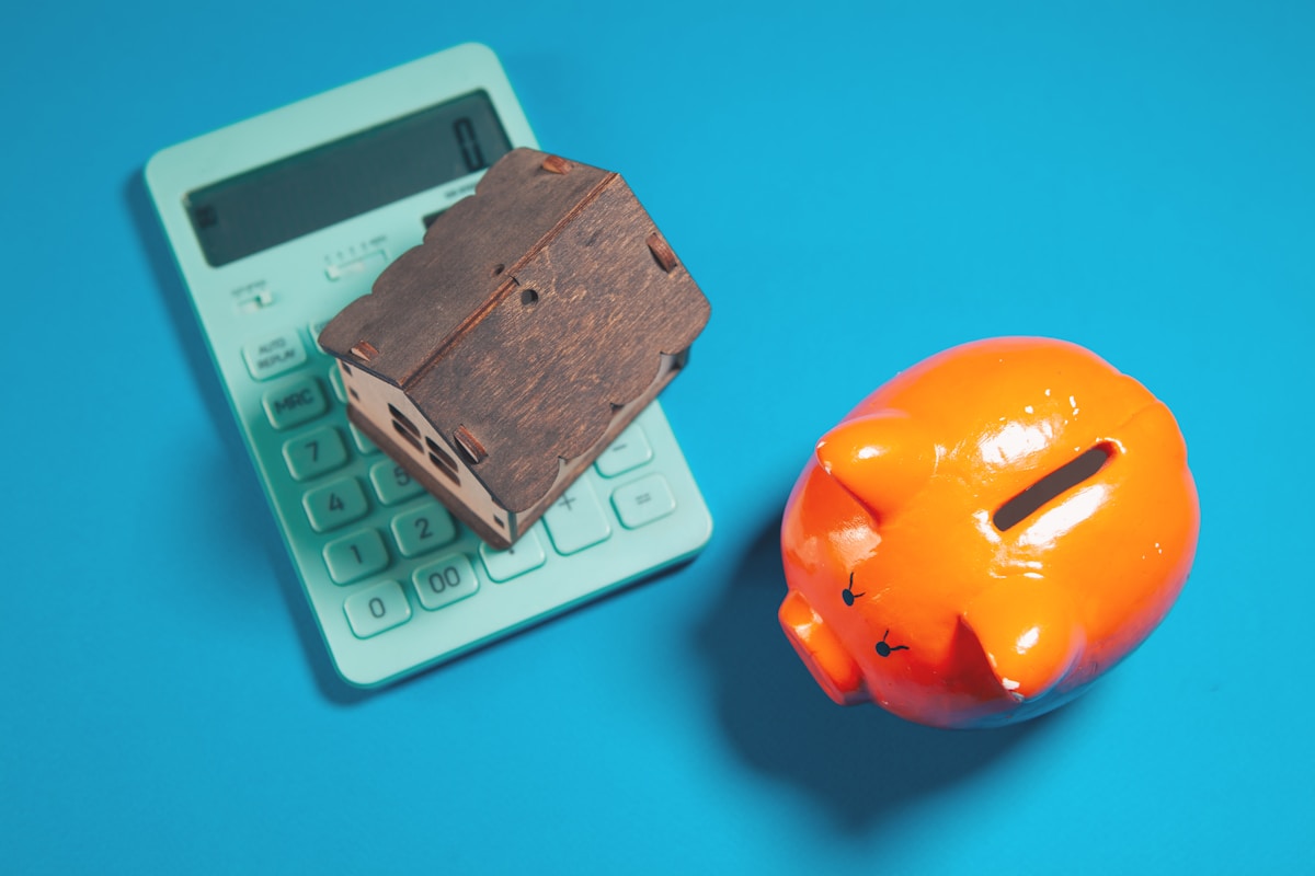 Calculatrice verte, tirelire en bois, fond bleu.