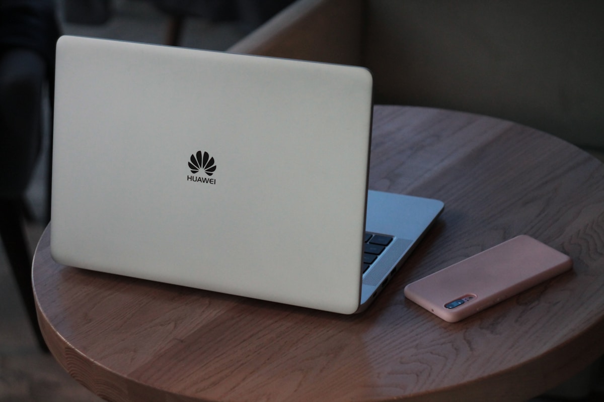 Ordinateur portable Huawei blanc sur une table en bois avec un téléphone rose.