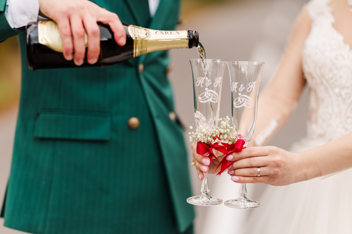 Couple en tenue de mariage, champagne versé dans des flûtes décorées.