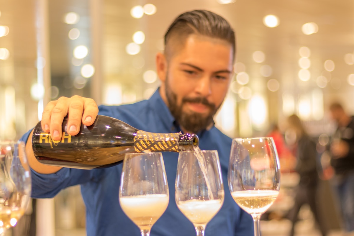 Barman versant du vin dans des verres à vin sur fond lumineux.