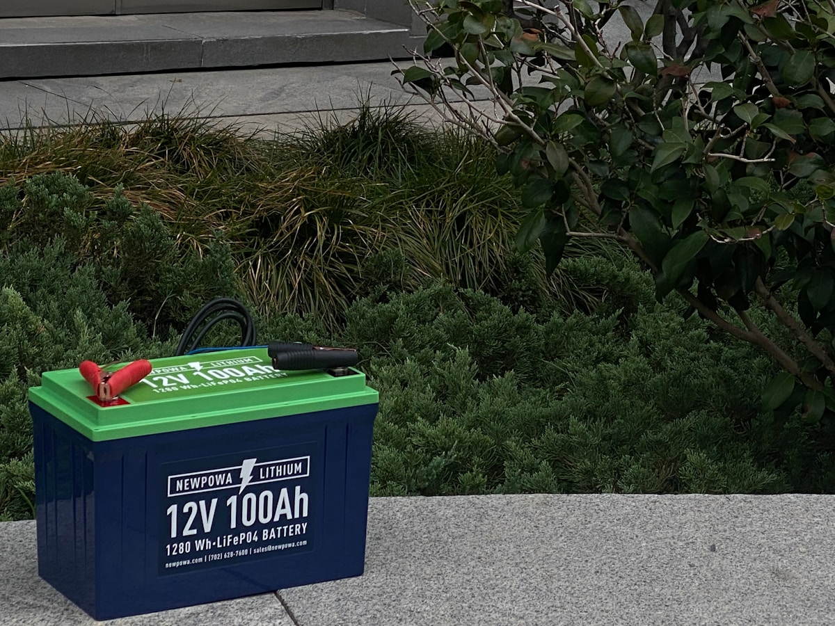 Batterie lithium-ion verte et bleue de 12V 100Ah sur un sol de pierre.