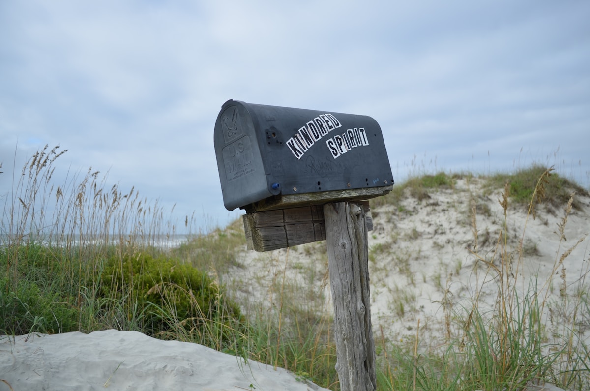 Boîte aux lettres noire sur un poteau en bois dans un paysage côtier.