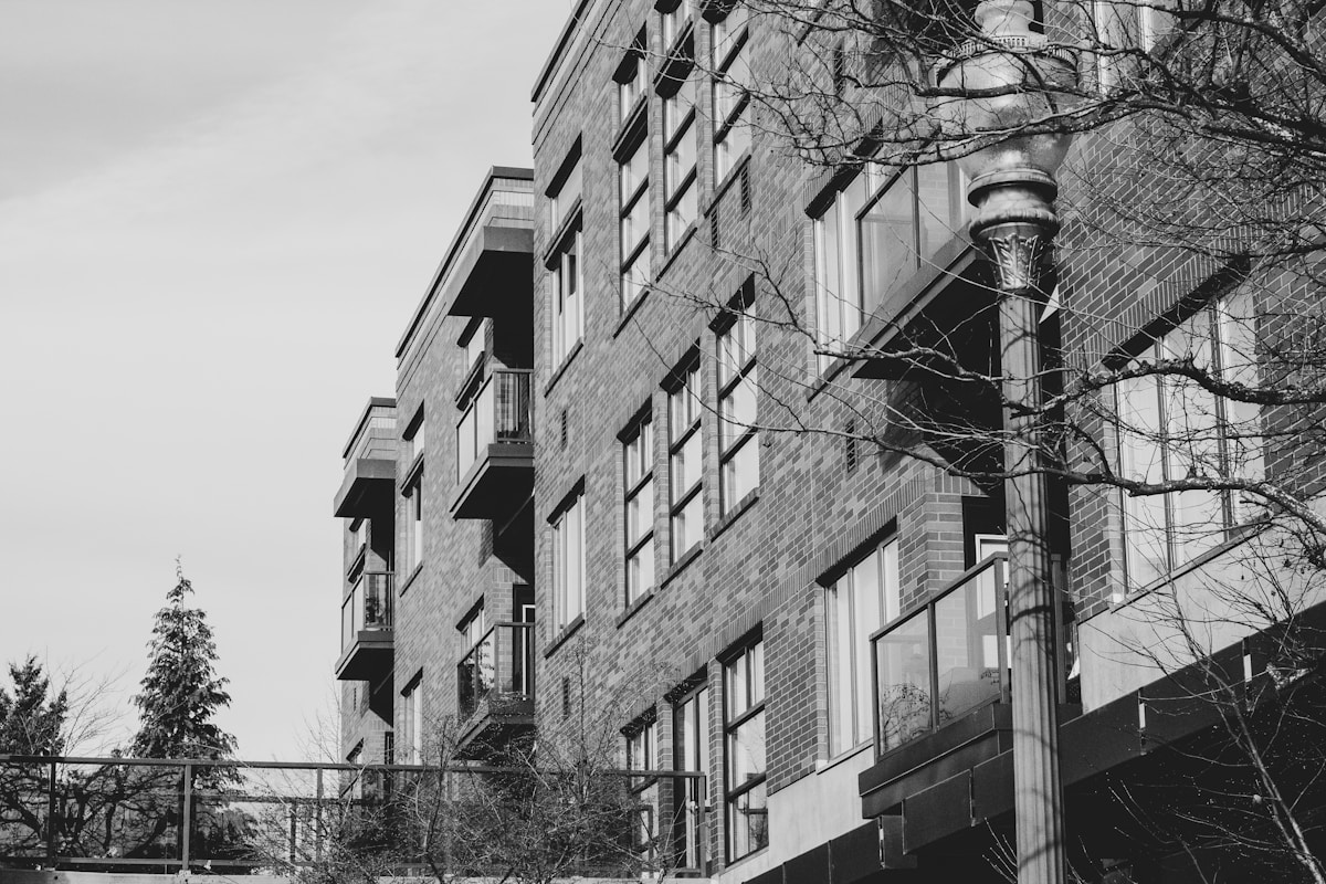 Bâtiment en briques, fenêtres, balcons, lampadaire, arbres nus.