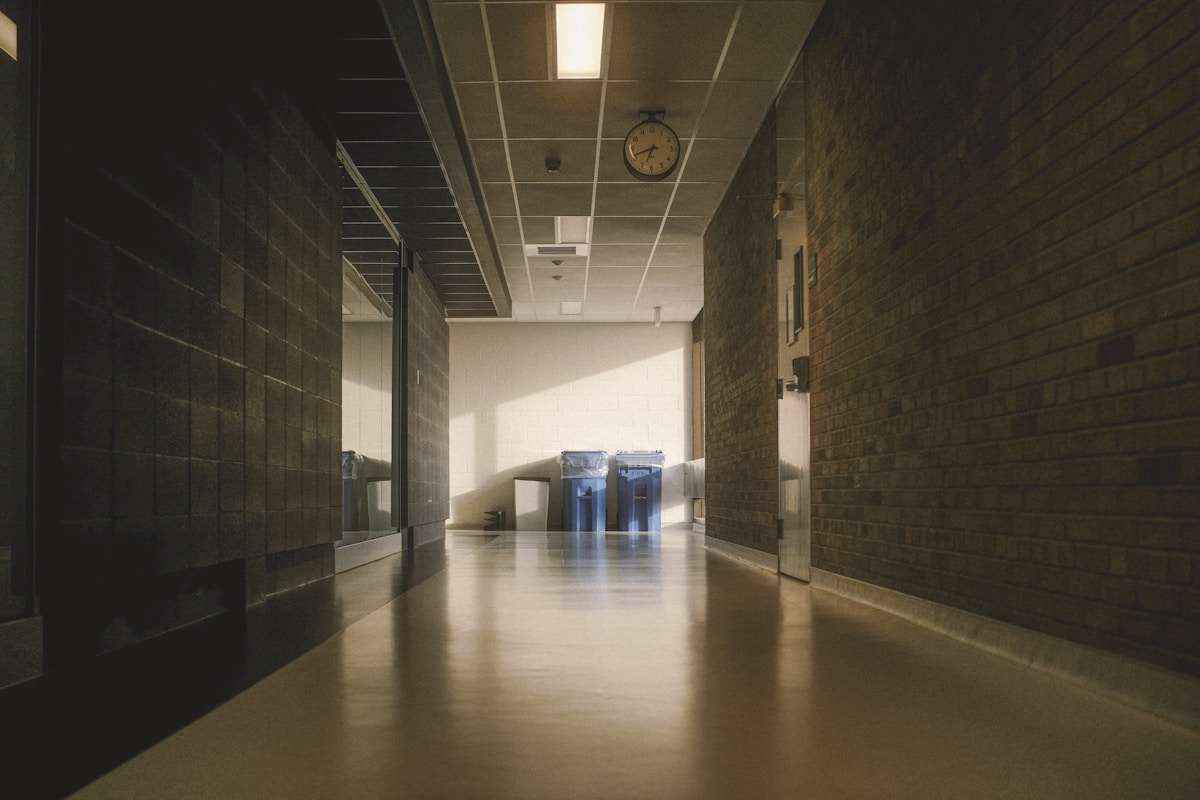 Couloir sombre et vide d'un bâtiment, avec horloge et casiers.