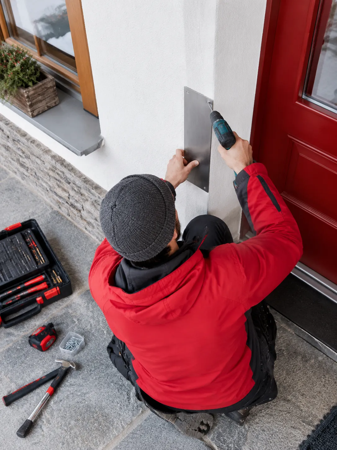 Technicien fixant une plaque métallique près d’une porte rouge