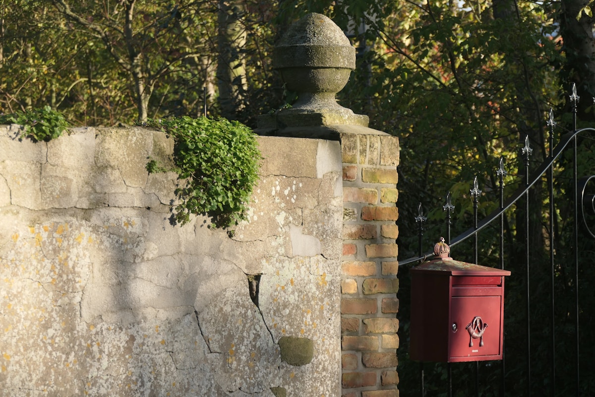 Mur de pierre avec boîte aux lettres rouge, végétation verdoyante.