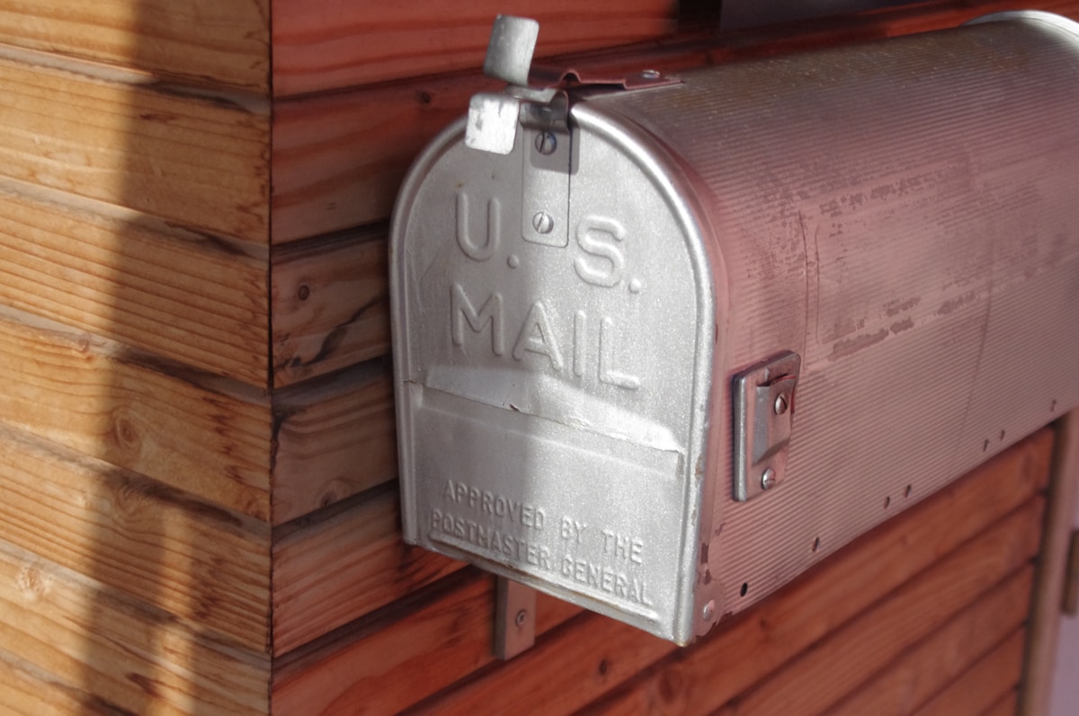 Boîte aux lettres postale en métal gris sur un mur en bois.