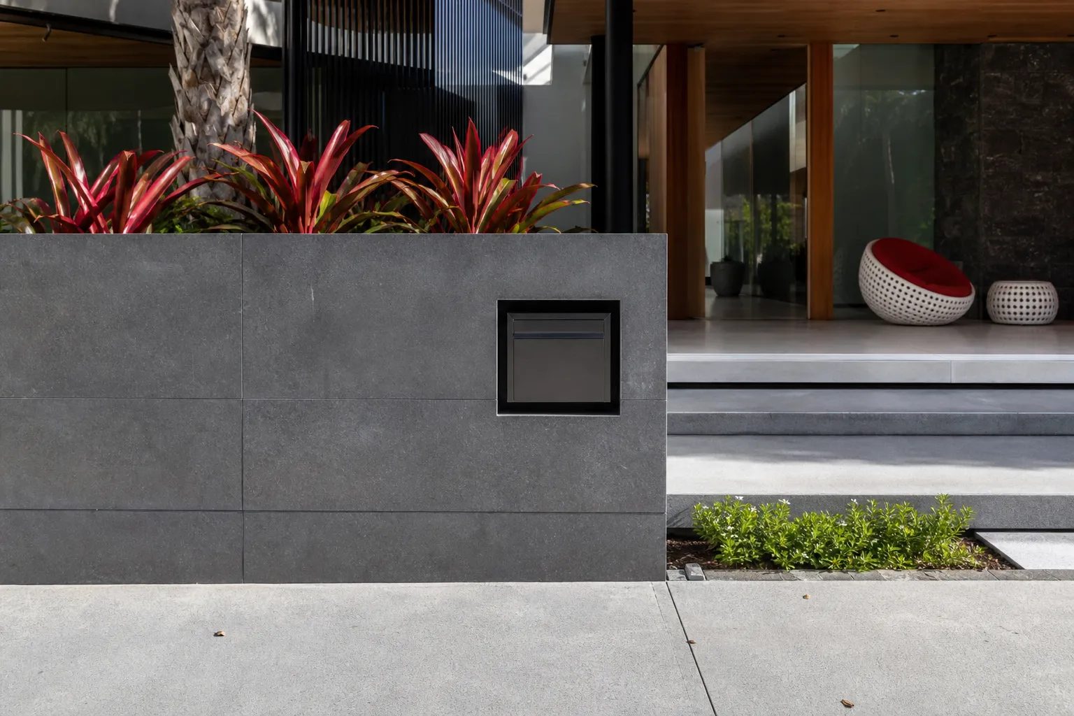 Entrée moderne avec plantes tropicales rouges et végétation verte.