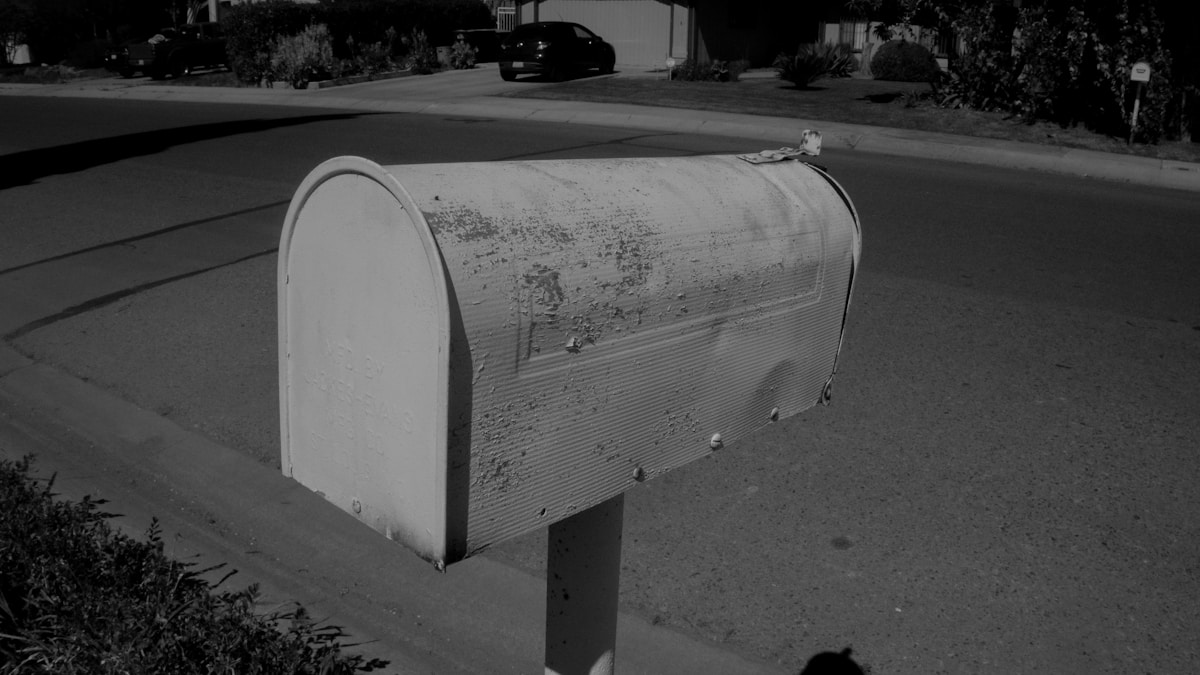 Boîte aux lettres blanche et rouillée sur le trottoir.