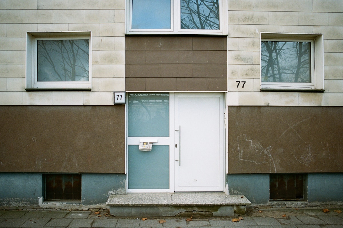 Immeuble résidentiel en briques beige, numéro 77, porte d'entrée blanche.