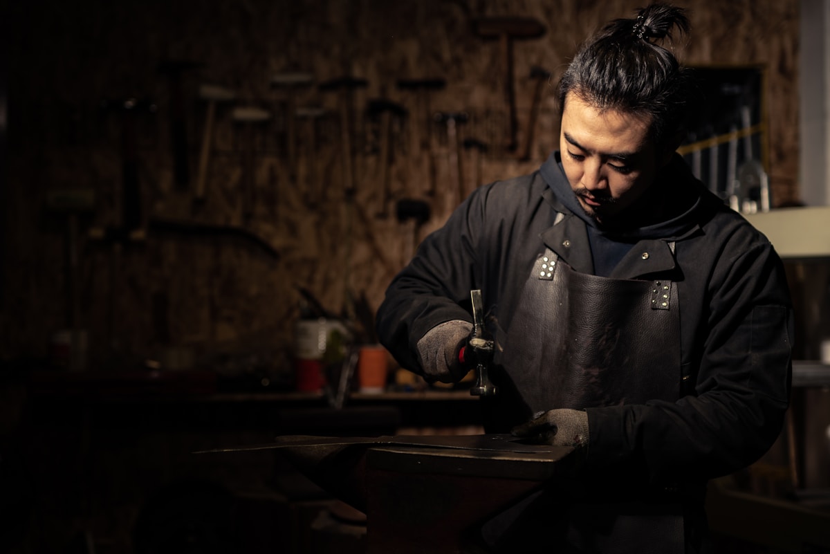 Artisan travaillant le métal dans un atelier sombre et rustique.