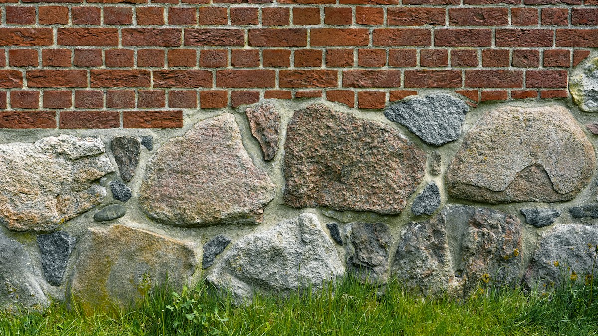 Mur en briques rouges et pierres irrégulières, herbe au premier plan