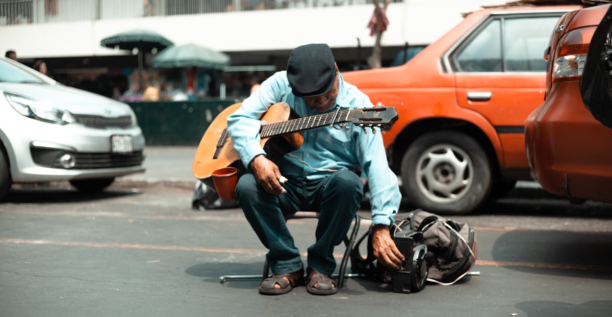 man sitting on street holding guitar