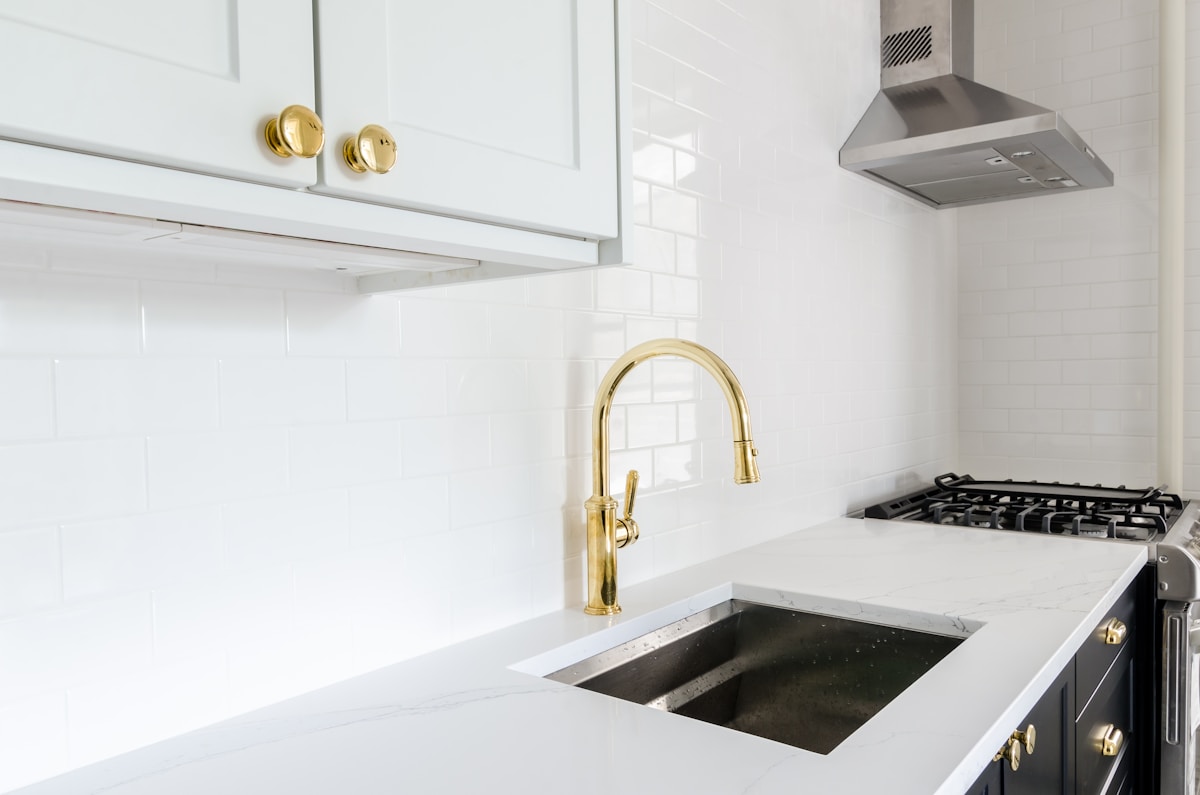 Cuisine moderne avec armoires blanches, robinet doré et électroménagers en acier inoxydable.