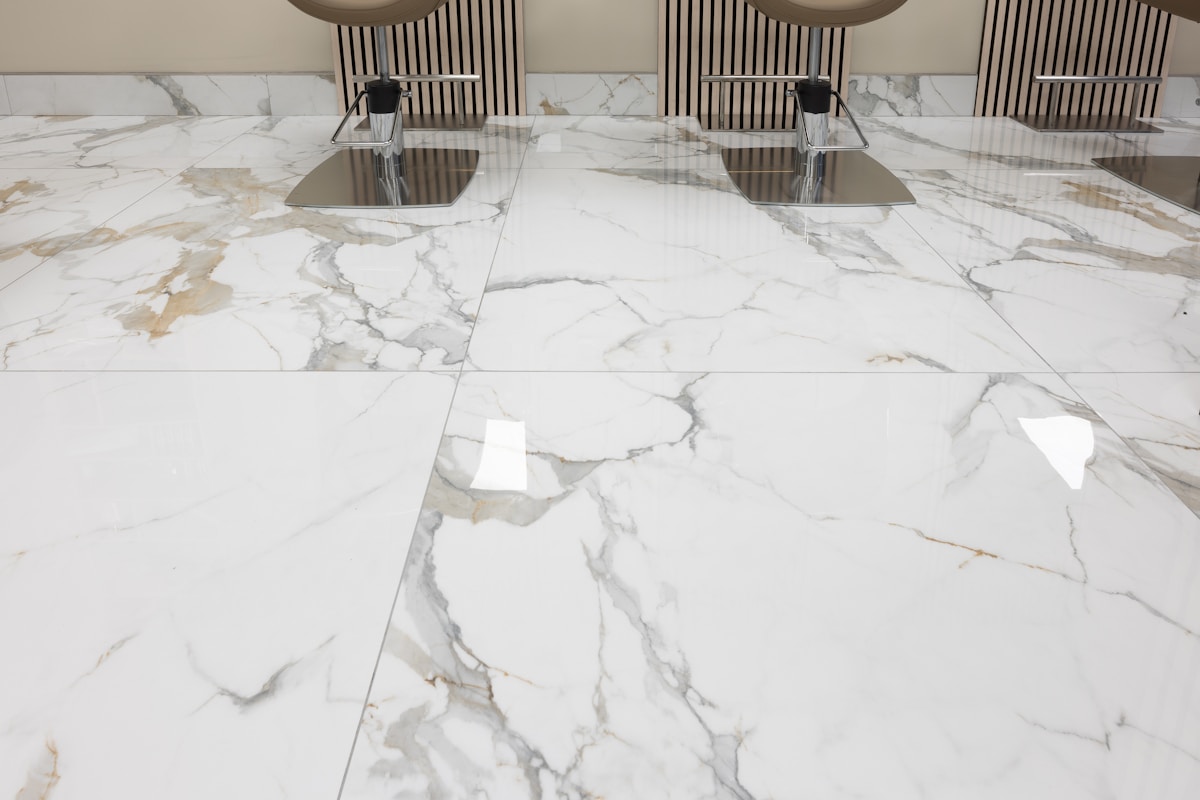 Carrelage de marbre blanc veiné, comptoir en métal brillant, luminaires suspendus.