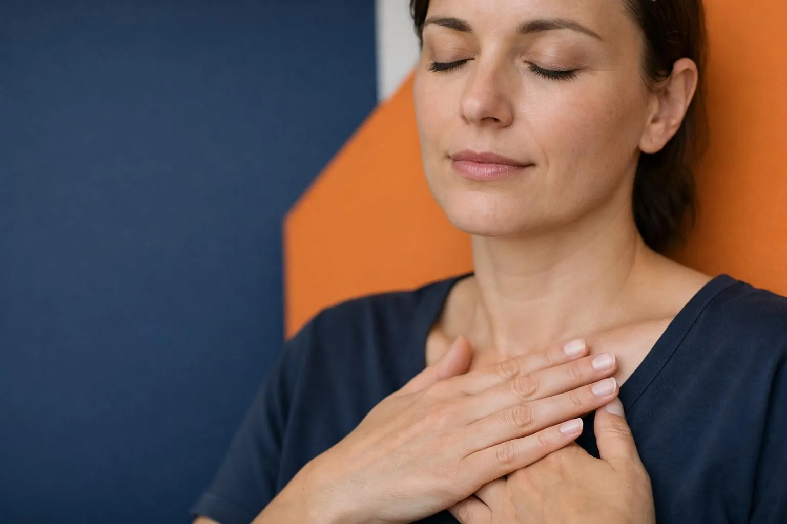 Close-up of person's hand gently touching their chest area with contemplative expression, eyes closed, representing the connection between emotions and physical sensations in the body
