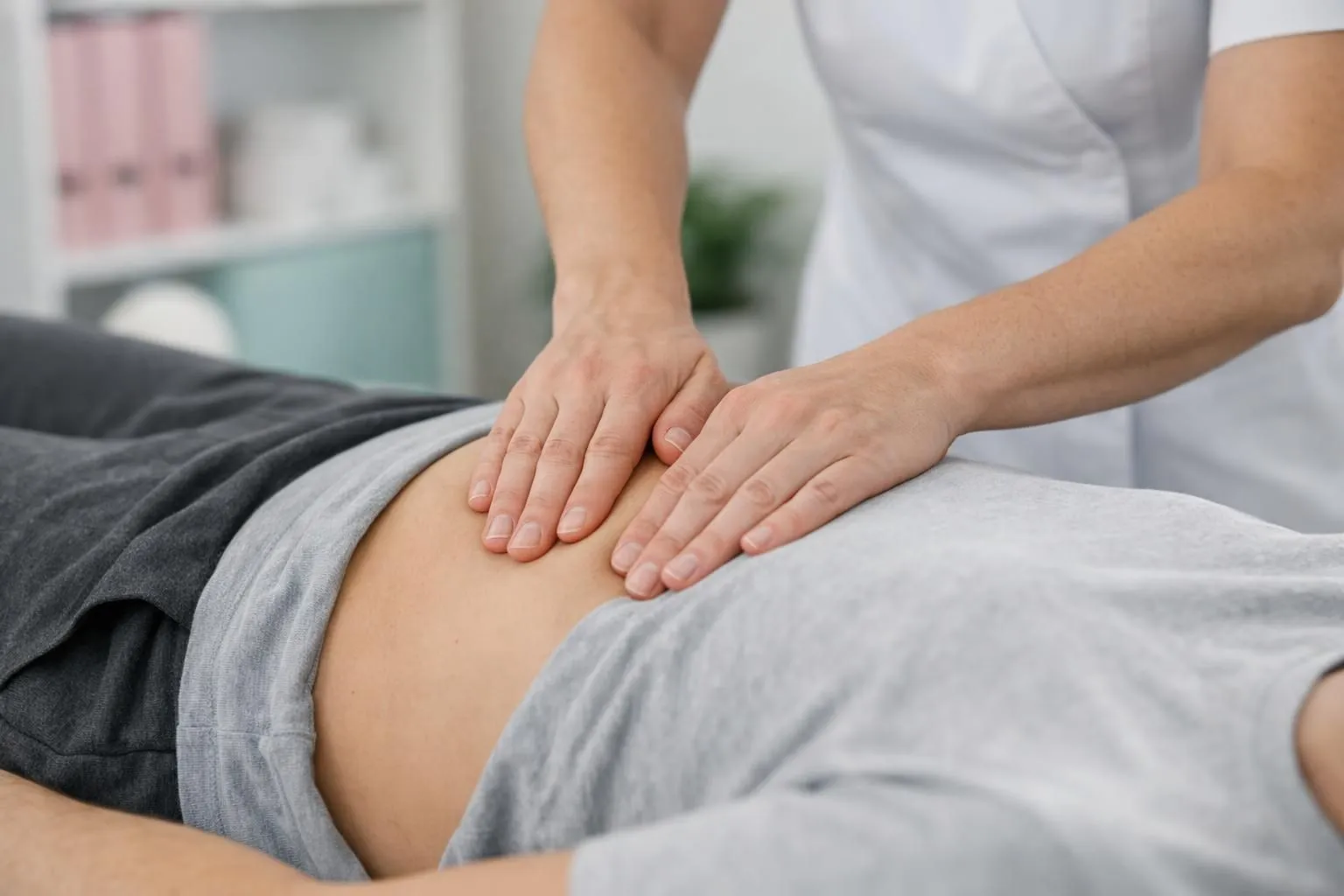 Osteopath's hands performing gentle visceral manipulation on patient's abdomen in clinical setting, professional healthcare environment, therapeutic touch technique, patient lying comfortably on treatment table