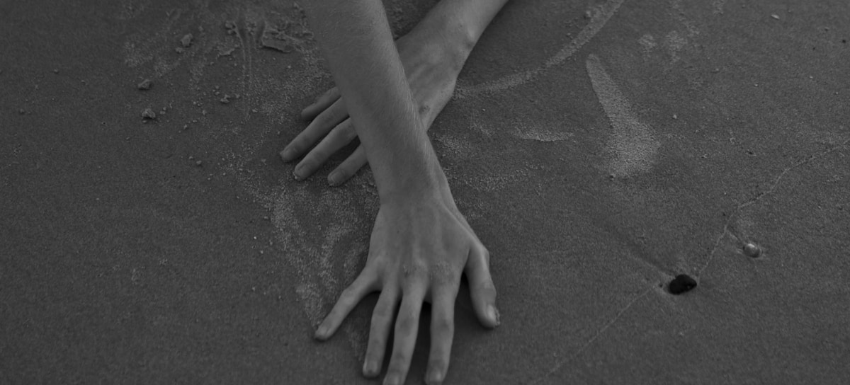a black and white photo of a person's hands in the sand