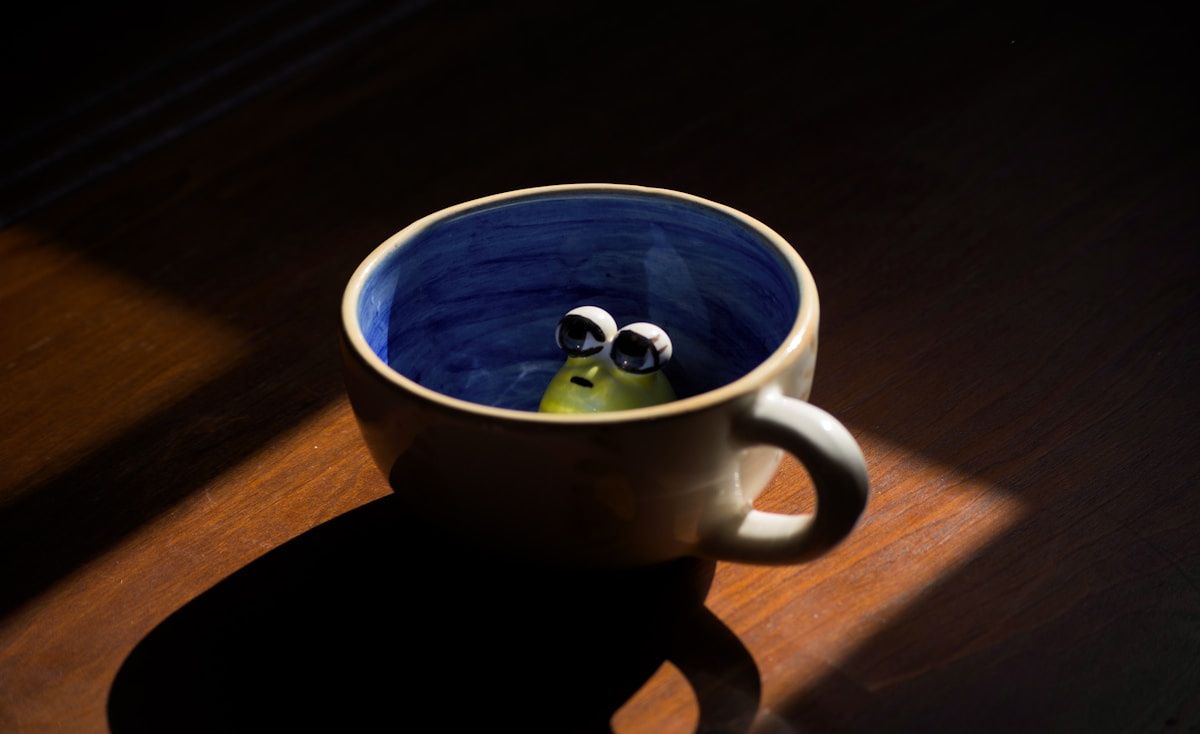 A small green frog peeking from a coffee cup