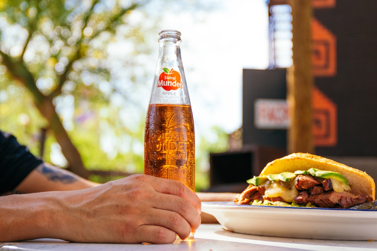 Une personne assise à une table avec un plat de nourriture et une bouteille de soda.