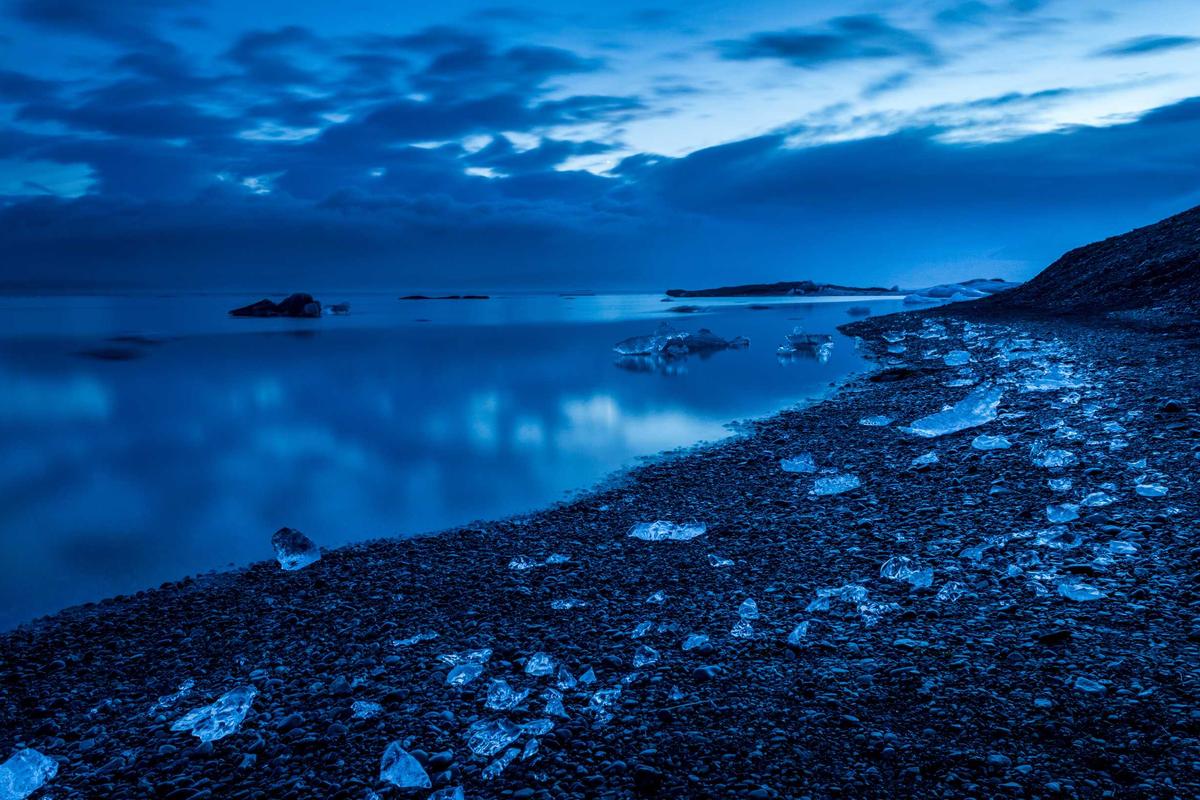 Serene blue lake surrounded by rocky shoreline and dramatic clouds.