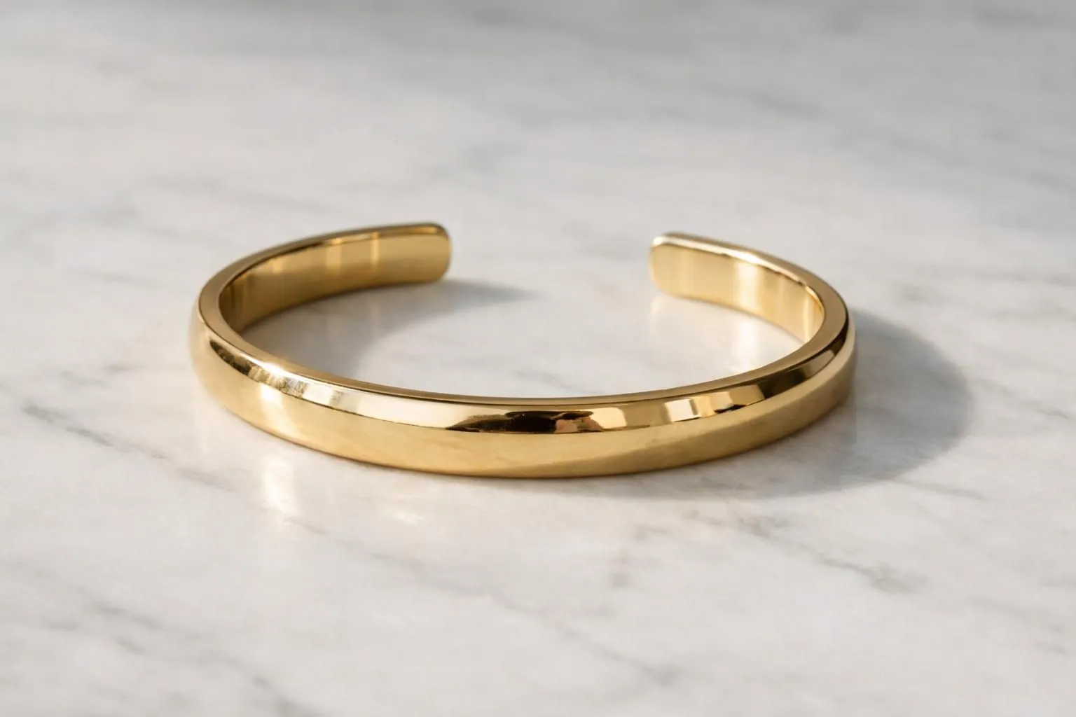 Elegant solid gold cuff bracelet displayed on luxurious white marble surface with dramatic side lighting revealing thickness and fine craftsmanship details, jewelry photography style