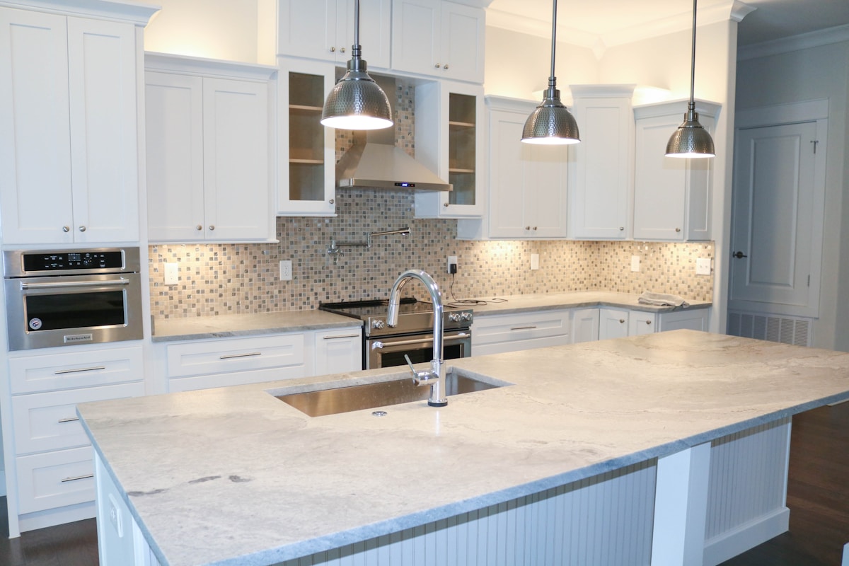 Cuisine moderne avec armoires blanches, comptoirs en marbre et luminaires suspendus.