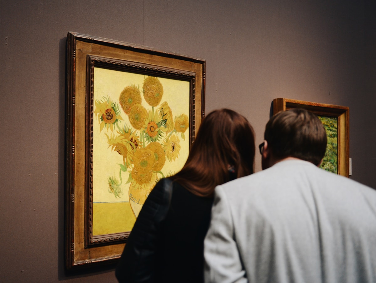 Deux personnes admirant un tableau de tournesols de Van Gogh dans une galerie.