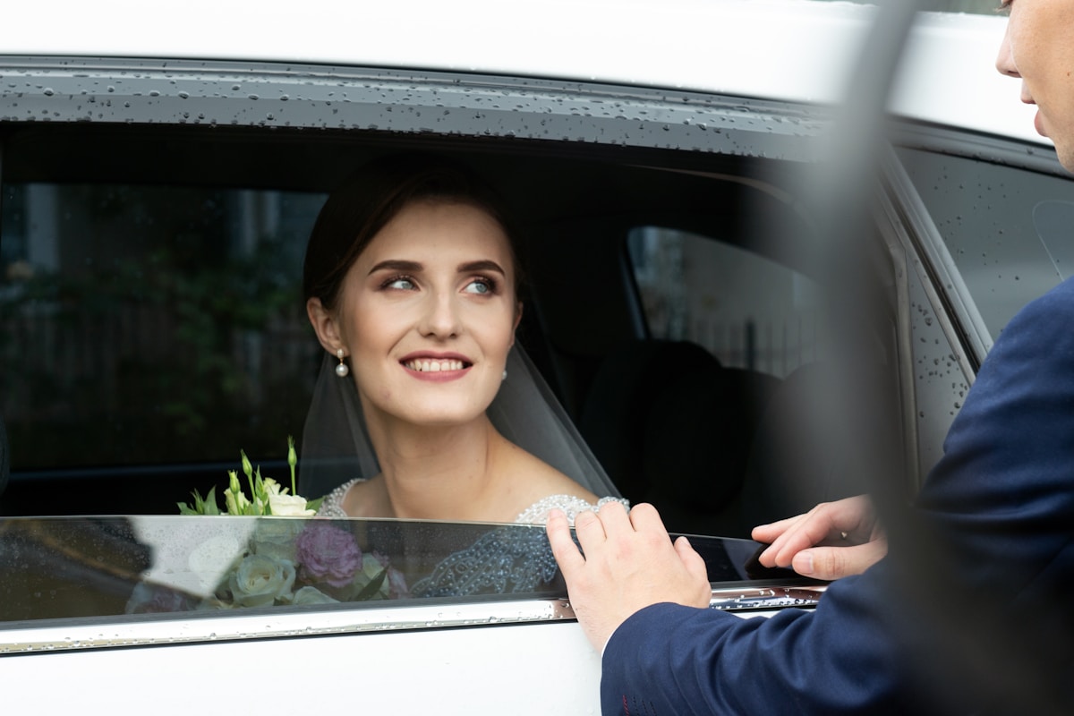 Mujer con vestido de novia dentro de un coche sonriendo