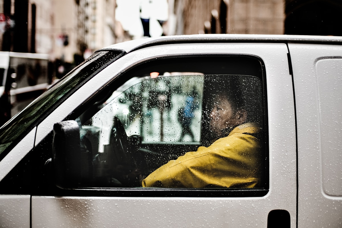 Voiture blanche par temps pluvieux avec une personne en veste jaune à l'intérieur.