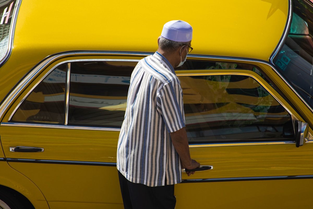 Homme en tenue traditionnelle près d'un taxi jaune.